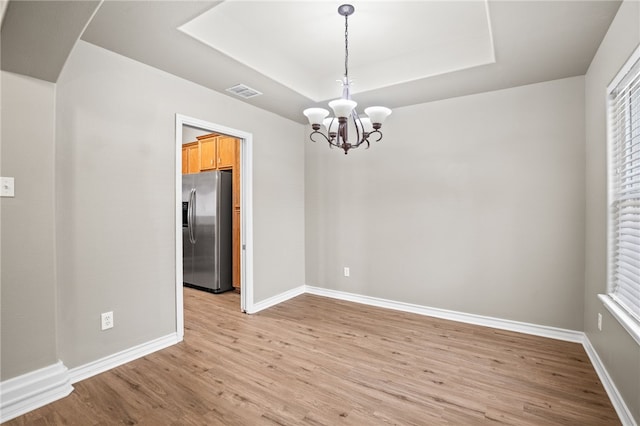 spare room featuring an inviting chandelier, light wood-type flooring, and a tray ceiling