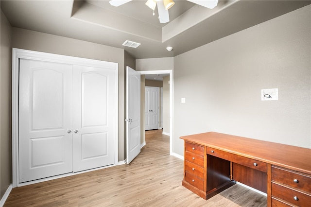 unfurnished office with light hardwood / wood-style floors, ceiling fan, and a tray ceiling