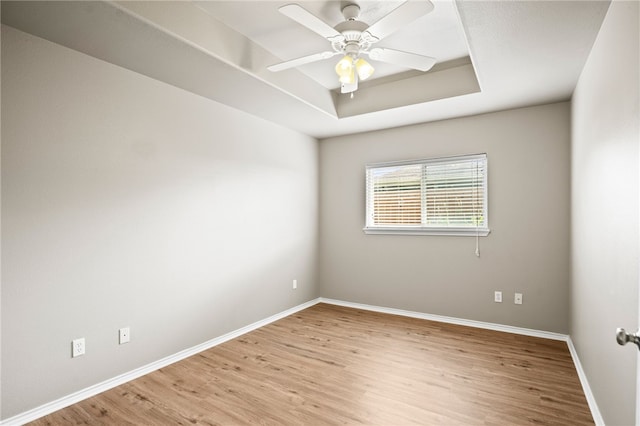 empty room featuring light hardwood / wood-style flooring, ceiling fan, and a tray ceiling