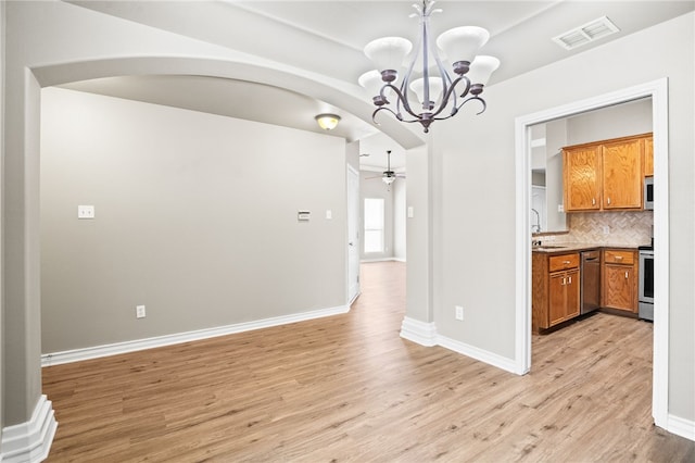 unfurnished dining area featuring ceiling fan with notable chandelier, sink, and light wood-type flooring