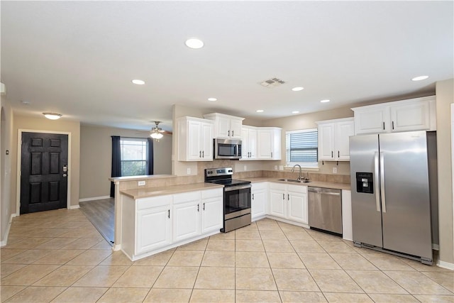 kitchen featuring light tile patterned flooring, sink, kitchen peninsula, stainless steel appliances, and white cabinets