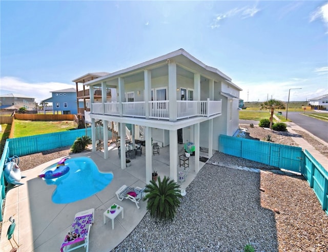 rear view of property featuring a fenced in pool, a balcony, and a patio area