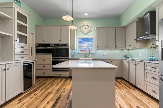 kitchen with wine cooler, a kitchen island, hanging light fixtures, wall chimney exhaust hood, and light hardwood / wood-style flooring