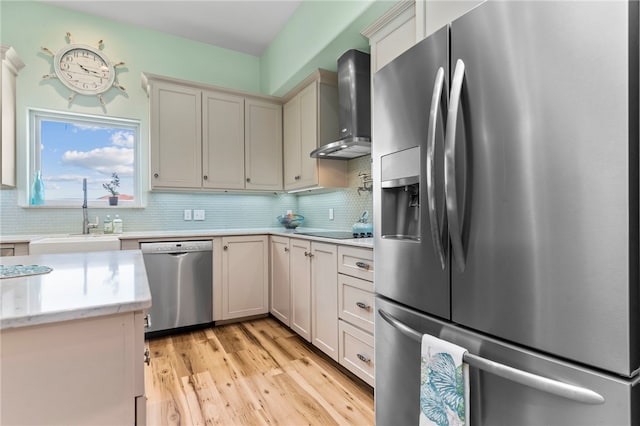 kitchen featuring stainless steel appliances, sink, tasteful backsplash, wall chimney range hood, and light hardwood / wood-style flooring