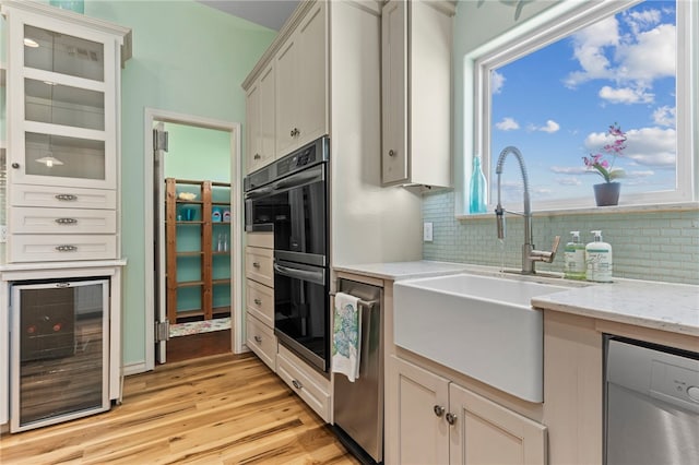 kitchen featuring beverage cooler, light hardwood / wood-style floors, stainless steel dishwasher, and a healthy amount of sunlight