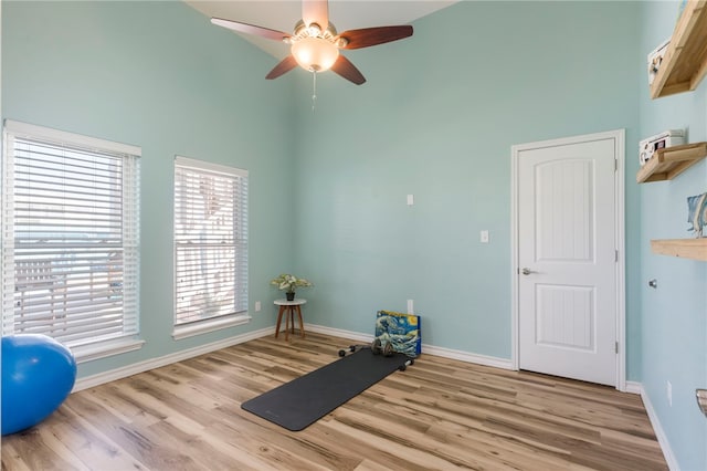 workout room with a towering ceiling, light wood-type flooring, a healthy amount of sunlight, and ceiling fan