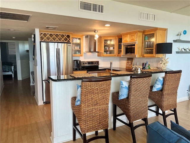 kitchen with stainless steel appliances, a breakfast bar, kitchen peninsula, wall chimney range hood, and light wood-type flooring