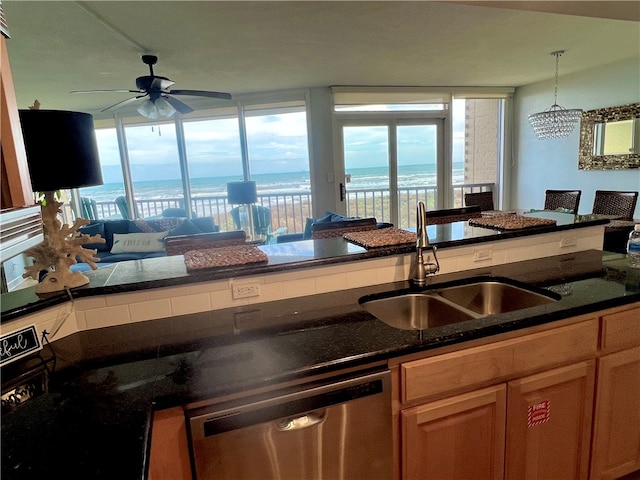 kitchen with sink, a water view, dark stone counters, ceiling fan with notable chandelier, and dishwasher