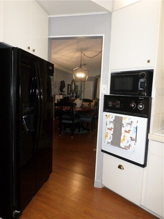 kitchen featuring wood-type flooring, hanging light fixtures, black appliances, a notable chandelier, and white cabinetry