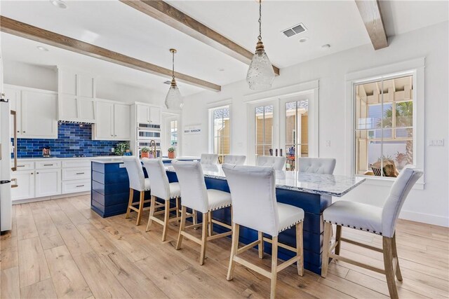 dining area with light wood finished floors, visible vents, baseboards, beamed ceiling, and french doors