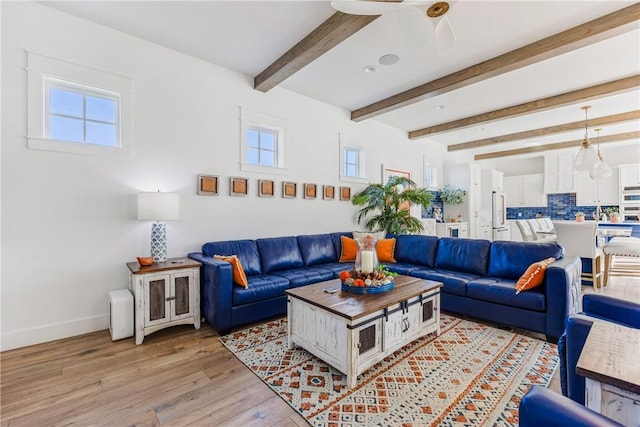 living room with light wood finished floors, beam ceiling, a healthy amount of sunlight, and baseboards