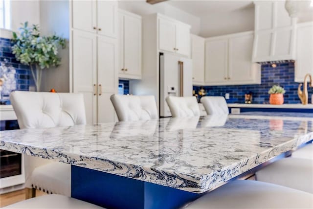 kitchen featuring backsplash, a breakfast bar area, light stone counters, white refrigerator with ice dispenser, and white cabinets