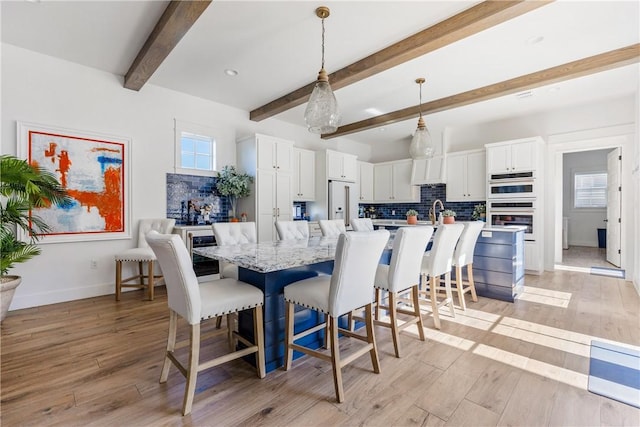 dining room featuring beam ceiling, a healthy amount of sunlight, baseboards, and light wood finished floors