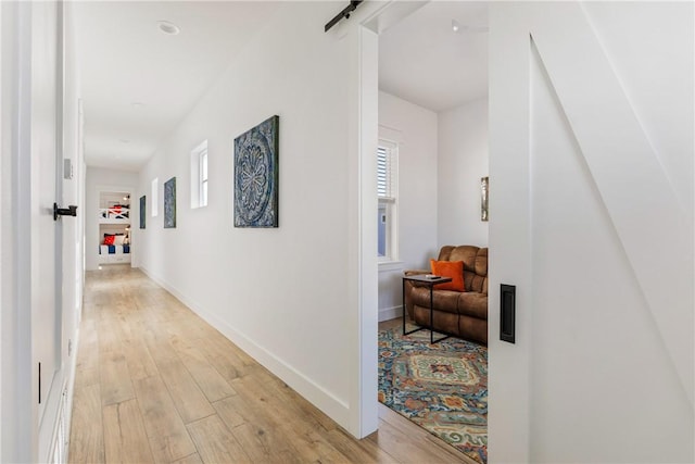 corridor featuring a barn door, light wood-style floors, and baseboards