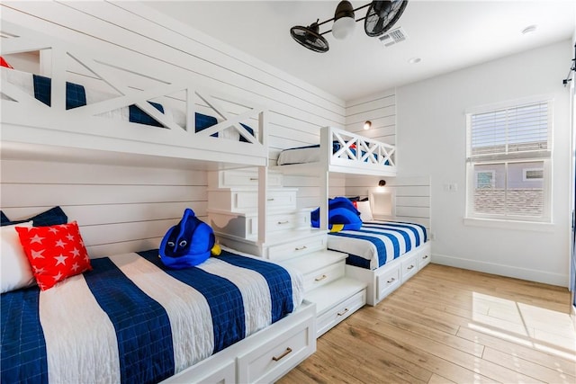 bedroom featuring visible vents, baseboards, light wood-style floors, and wooden walls