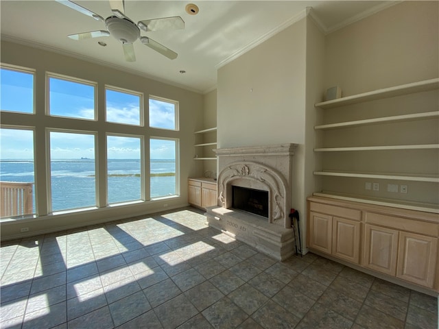 unfurnished living room featuring a fireplace, built in features, a water view, and ornamental molding