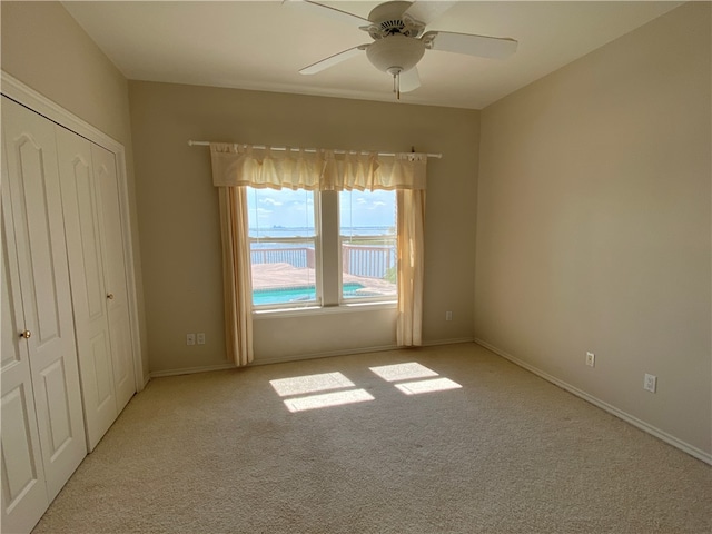 unfurnished bedroom featuring ceiling fan, light colored carpet, a closet, and a water view