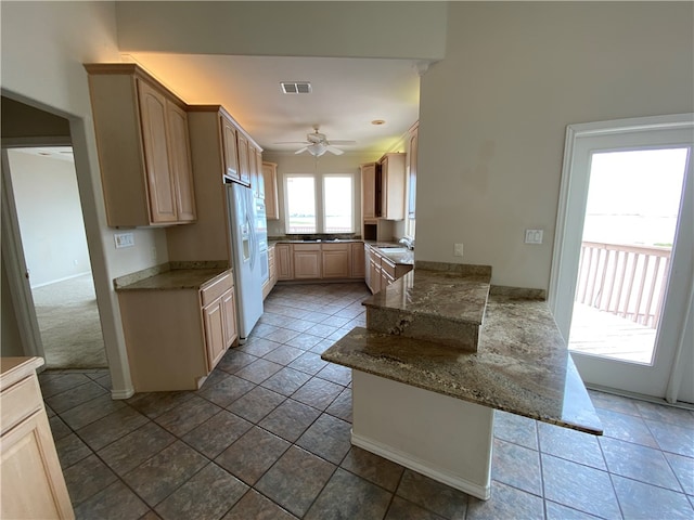 kitchen featuring sink, white refrigerator with ice dispenser, ceiling fan, stone countertops, and light brown cabinetry