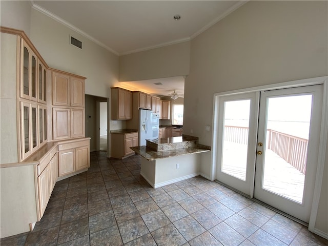 kitchen featuring kitchen peninsula, a towering ceiling, ornamental molding, white fridge with ice dispenser, and light brown cabinets