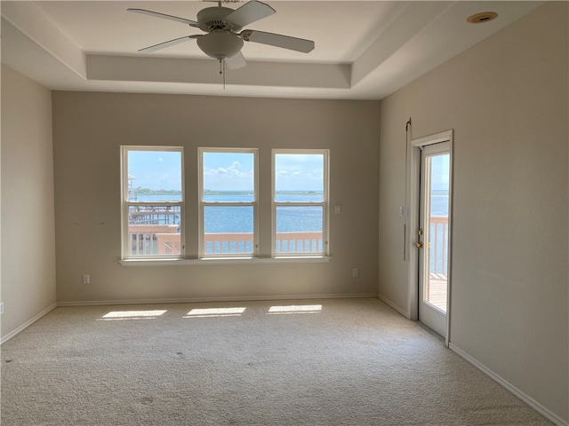 empty room featuring ceiling fan, a wealth of natural light, light colored carpet, and a water view