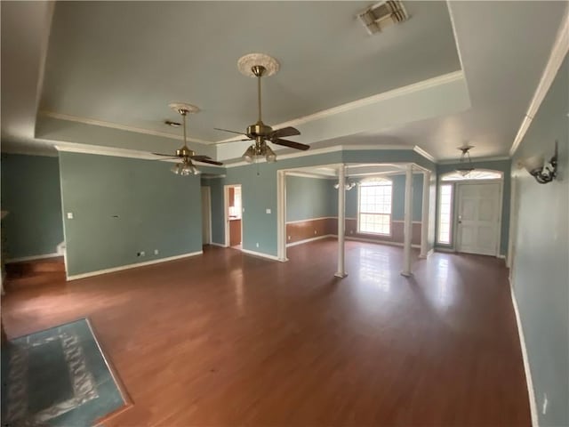 unfurnished living room featuring dark wood-type flooring, ceiling fan, ornamental molding, and a raised ceiling