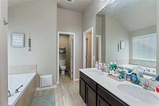 bathroom featuring lofted ceiling, toilet, hardwood / wood-style flooring, vanity, and a relaxing tiled tub