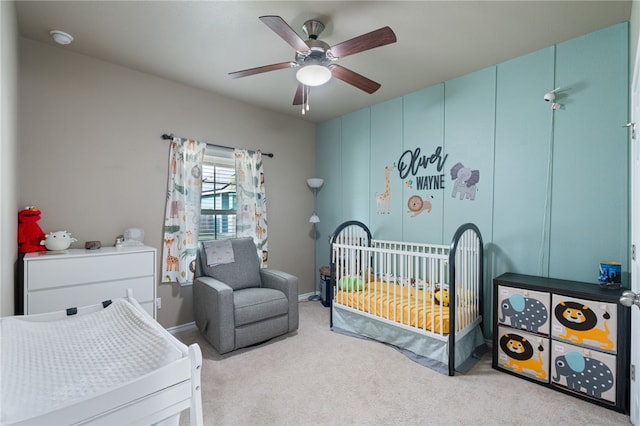 bedroom with a nursery area, ceiling fan, and light colored carpet