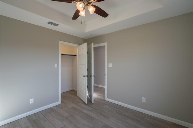unfurnished bedroom with baseboards, a tray ceiling, wood finished floors, and visible vents