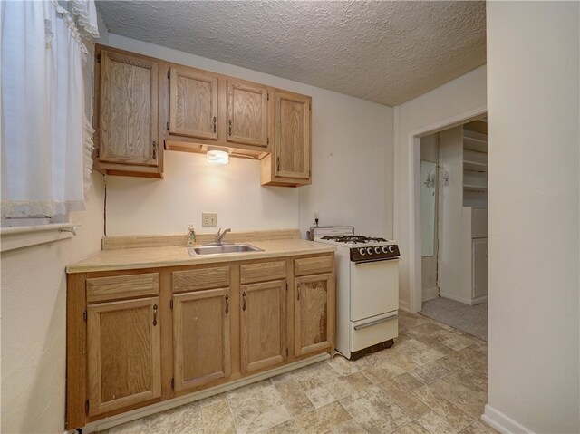 kitchen featuring white stove, light brown cabinetry, sink, and a textured ceiling