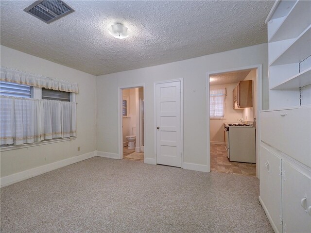 unfurnished bedroom with connected bathroom, light carpet, and a textured ceiling