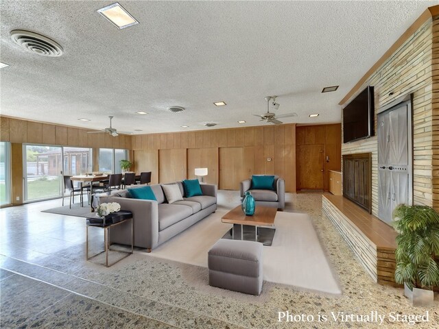 living room with wood walls, a textured ceiling, and ceiling fan