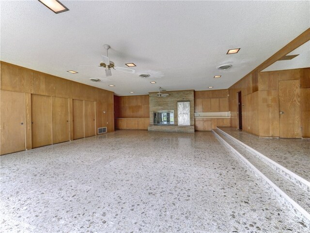 empty room with wood walls, a large fireplace, a textured ceiling, and ceiling fan