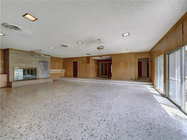 unfurnished living room featuring wood walls, ceiling fan, plenty of natural light, and a textured ceiling