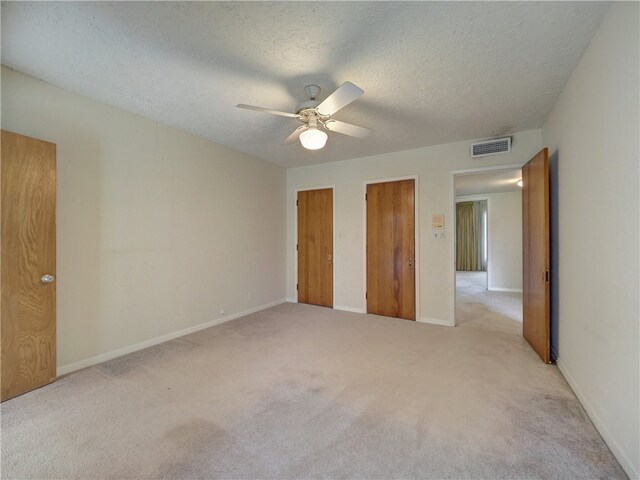 unfurnished bedroom with two closets, light carpet, ceiling fan, and a textured ceiling