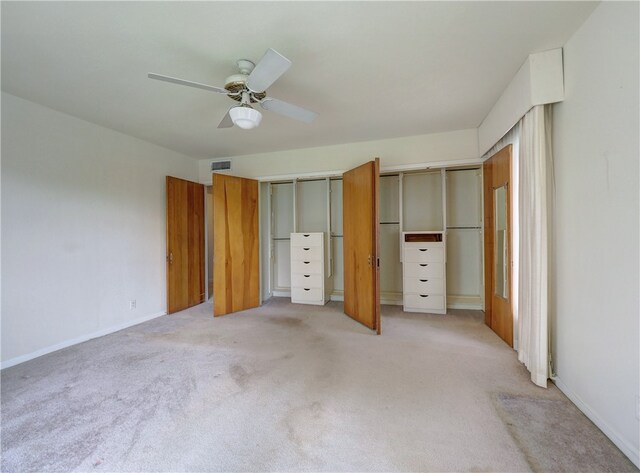 unfurnished bedroom featuring light carpet, ceiling fan, and two closets