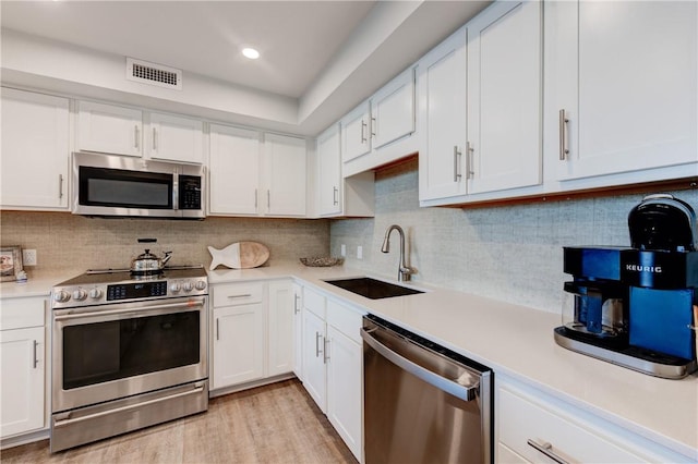 kitchen with stainless steel appliances, light hardwood / wood-style floors, backsplash, white cabinetry, and sink