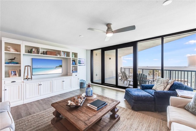 living room with a textured ceiling, a water view, ceiling fan, light hardwood / wood-style flooring, and floor to ceiling windows