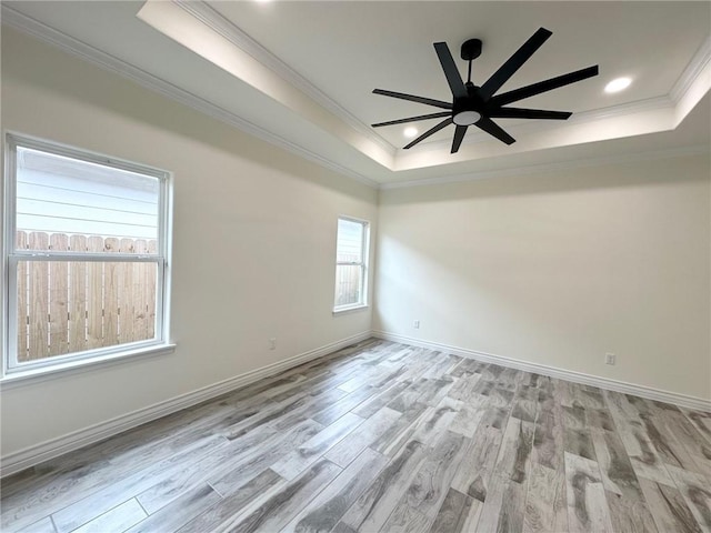 empty room featuring ceiling fan, baseboards, light wood-type flooring, a tray ceiling, and crown molding