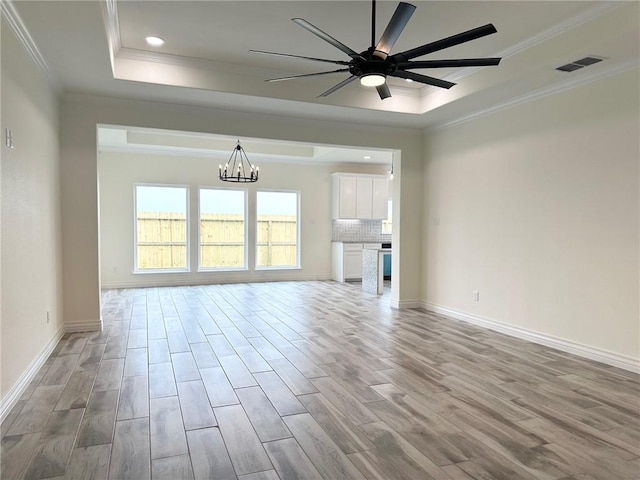 unfurnished living room with a tray ceiling, crown molding, visible vents, light wood-type flooring, and ceiling fan with notable chandelier