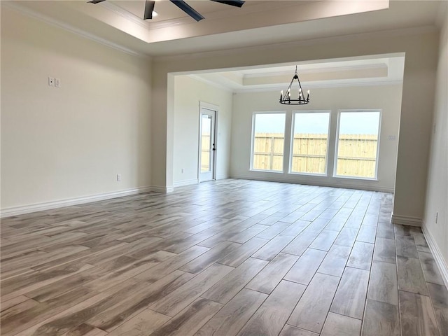 empty room featuring ornamental molding, wood finished floors, a raised ceiling, and baseboards