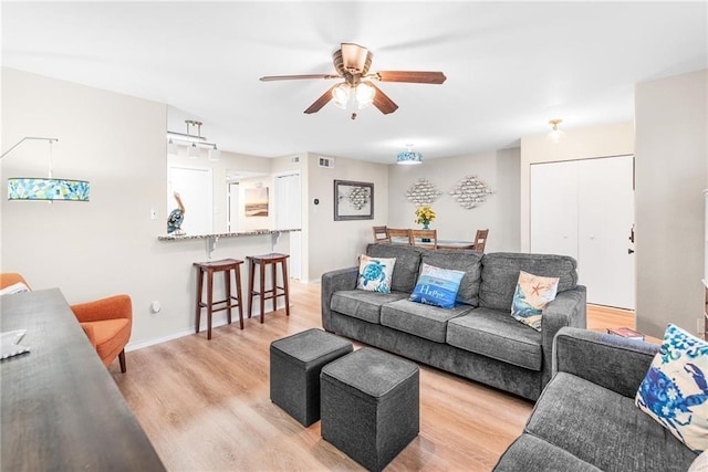 living room featuring ceiling fan, baseboards, visible vents, and light wood-style floors