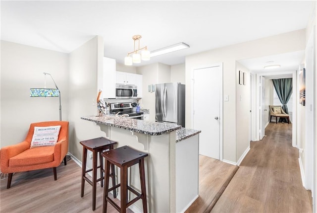 kitchen with appliances with stainless steel finishes, a peninsula, light stone countertops, a kitchen bar, and white cabinetry