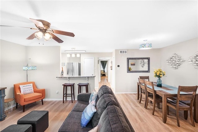 living area with ceiling fan, light wood finished floors, visible vents, and baseboards