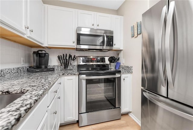 kitchen with light wood finished floors, decorative backsplash, appliances with stainless steel finishes, white cabinetry, and light stone countertops