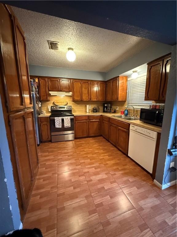 kitchen featuring brown cabinets, a sink, visible vents, light countertops, and appliances with stainless steel finishes