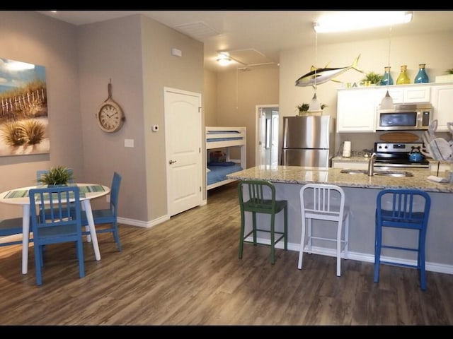 kitchen with light stone countertops, stainless steel appliances, white cabinets, dark hardwood / wood-style floors, and a breakfast bar area