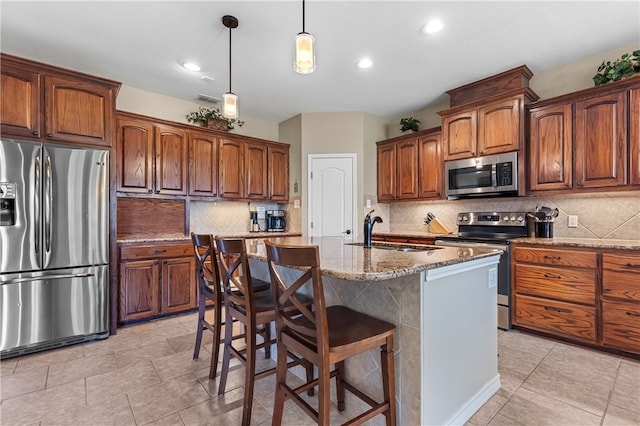 kitchen with a kitchen island with sink, sink, light stone countertops, decorative light fixtures, and stainless steel appliances