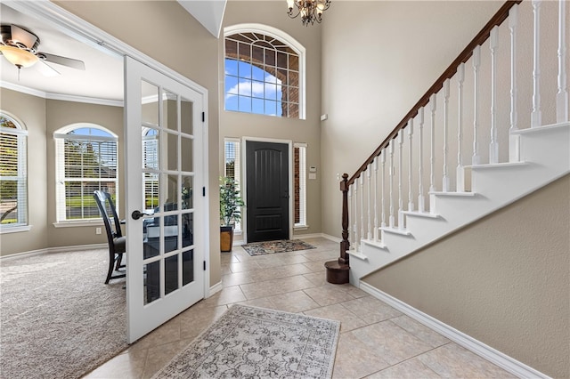 tiled entryway with french doors, a high ceiling, ceiling fan with notable chandelier, and ornamental molding