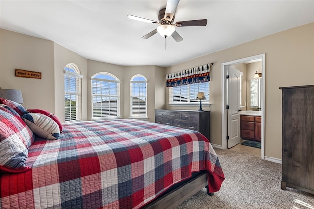 bedroom with ceiling fan, light colored carpet, and ensuite bath