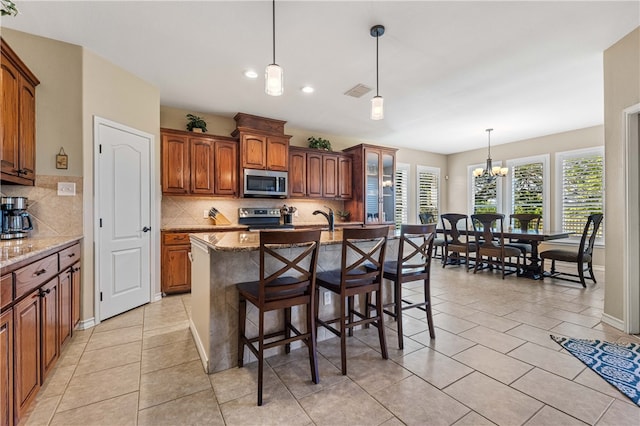 kitchen featuring light stone countertops, stainless steel appliances, hanging light fixtures, and an island with sink